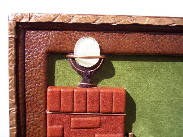 leather wall hanging detail with copper border, glass light on brick pillar, green suede background