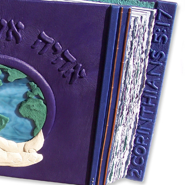 2 Corinthians 5:17 embossed under blue leather on custom book cover edge with hands holding earth