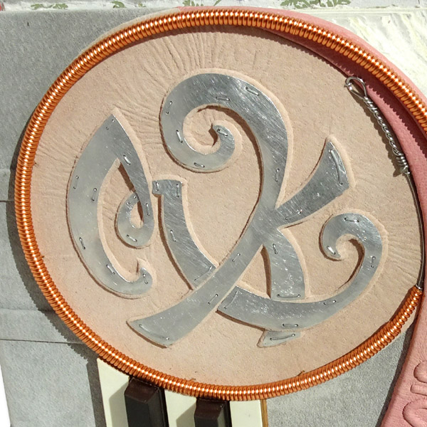 silver Monogram MK on pink and gray book cover with copper piano wire as circle frame